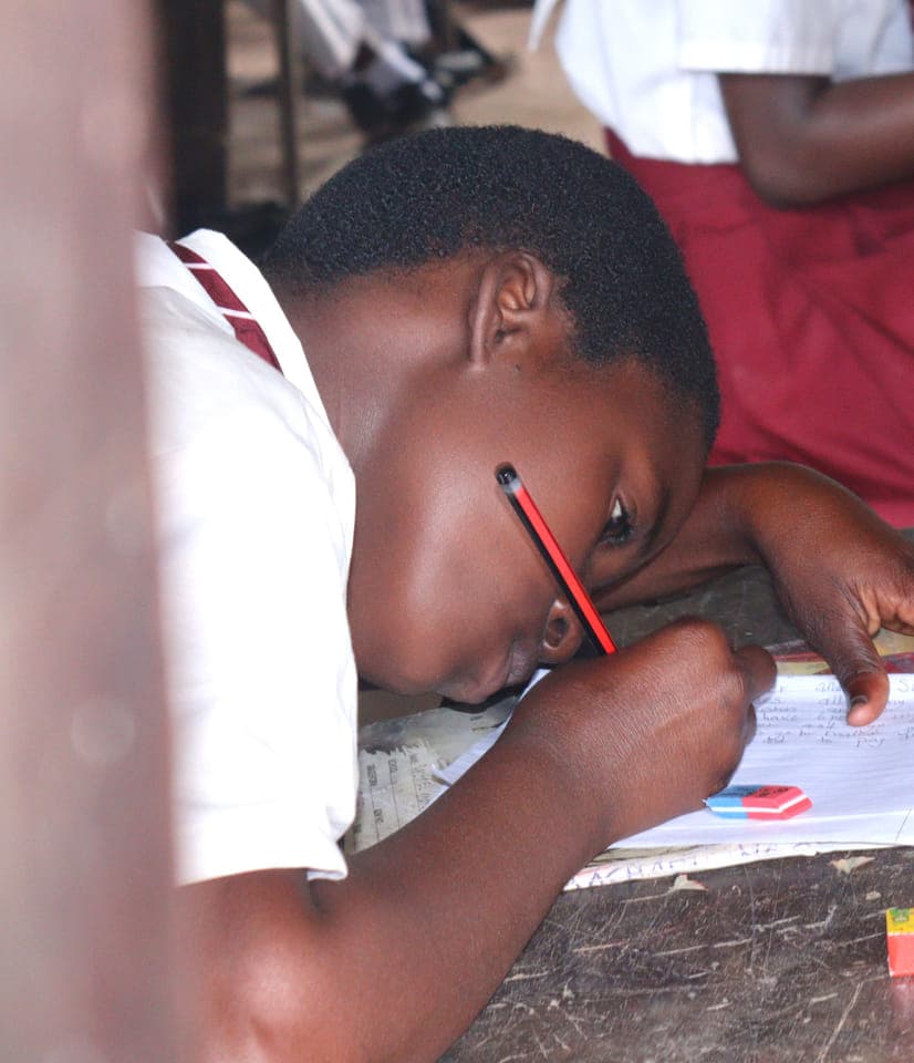 A Grade 7 learner writing an essay at Kiwegu